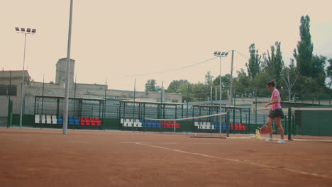 Closeup-footage-of-female-legs-in-sports-sneakers-and-prosthesis-on-her-leg-picking-up-tennis-balls-from-the-tennis-court-ground